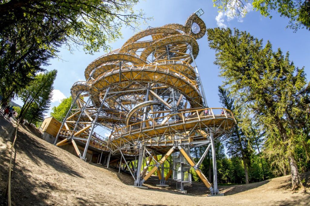 Zakręcony spiralnie wysoki taras widokowy usytułowany między drzewami.
