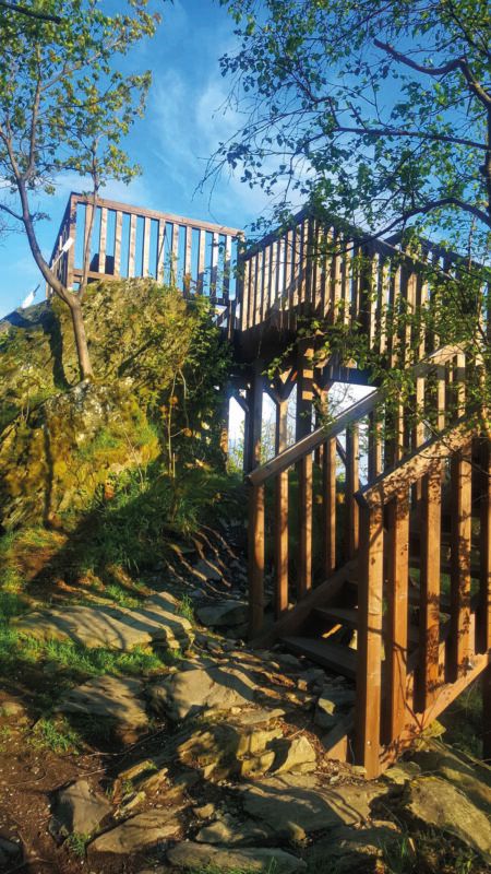 Widok na oświetlony promieniami słońca drewniany, niezadaszony taras widokowy na tle błękitnego nieba