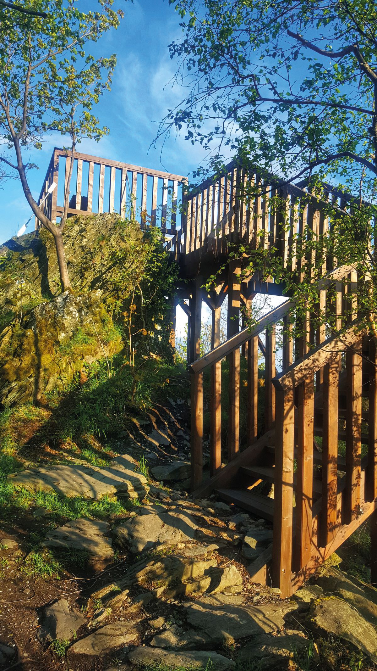 Widok na oświetlony promieniami słońca drewniany, niezadaszony taras widokowy na tle błękitnego nieba