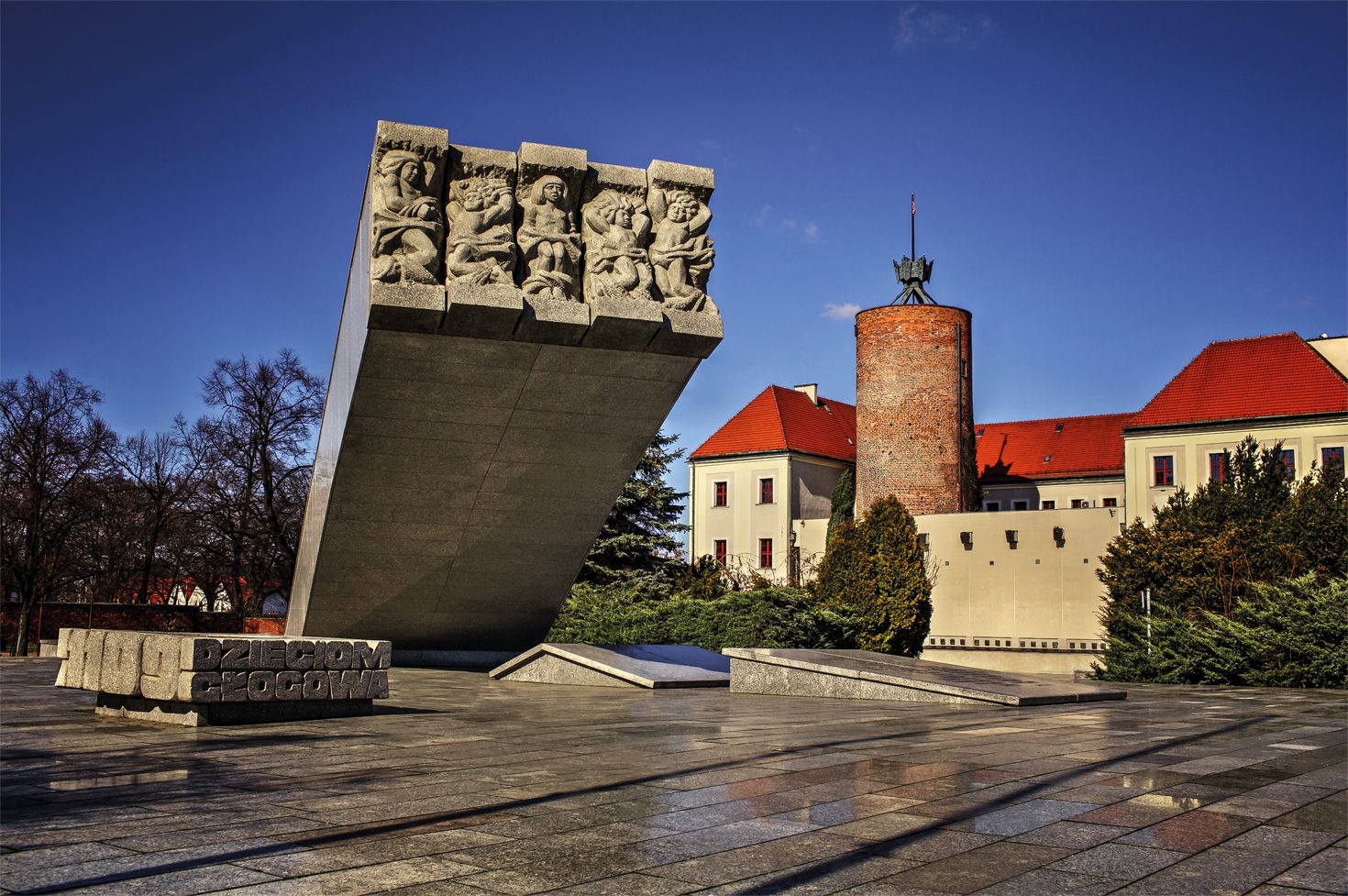Monumentalny pomnik z budynkiem Zamku Głogowskiego w tle przy ładnej pogodzie