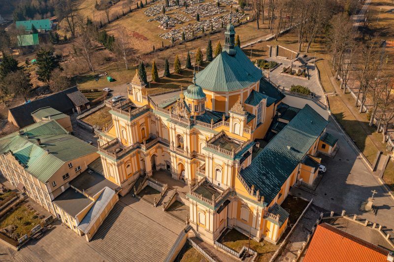 Na zdjęciu widać okazałe sanktuarium w Wambierzycach z monumentalnymi schodami prowadzącymi do barokowej fasady ozdobionej kolumnami i wieżami.