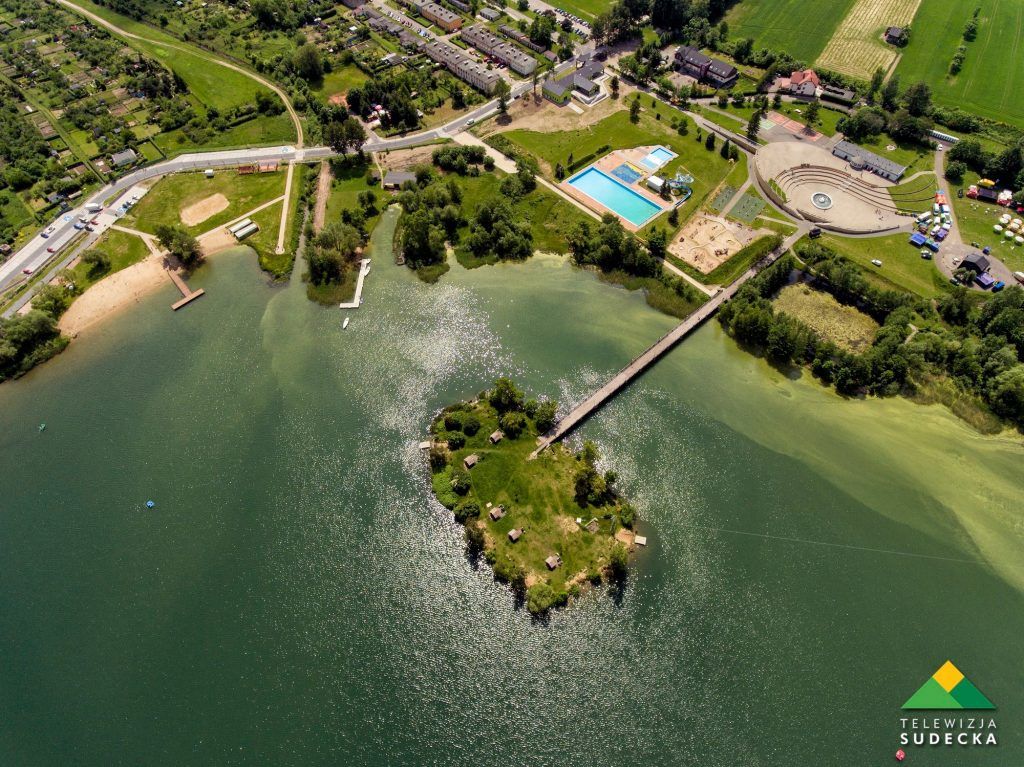 Widok z lotu ptaka na jezioro, otoczone zielenią, domkami