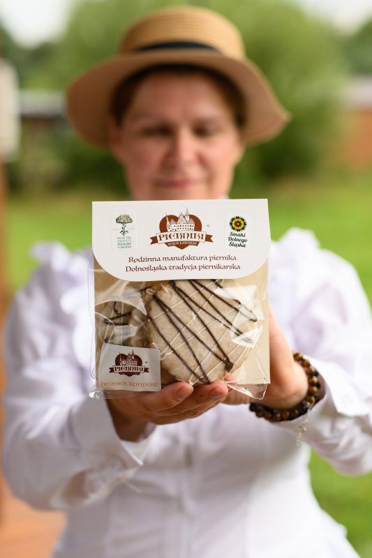 Kobieta w haftowanej koszuli i kapeluszu prezentuje zapakowane pierniki