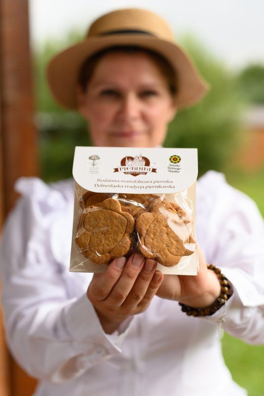 Kobieta w haftowanej koszuli i kapeluszu prezentuje zapakowane pierniki