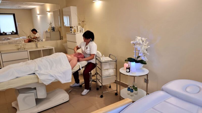 Gabinet zabiegowy. Personel kosmetyczny wykonuje zabieg na twarzy leżącego klienta.