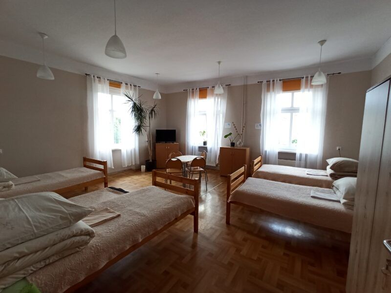 Wnętrze pokoju wieloosobowego pokoju noclegowego z 4 drewnianymi, łóżkami pojedynczymi.