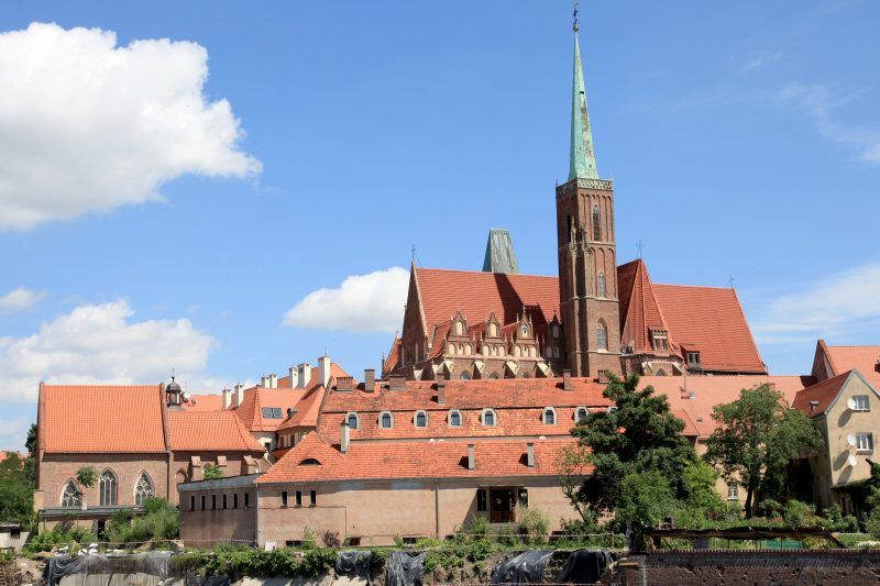 Widok na zabytkowe budynku pokryte czerwoną dachówką , w tle spiczasta wieża kościoła św. Marcina