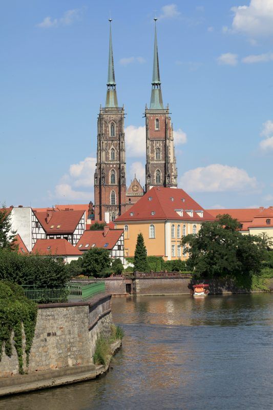 Przepływająca rzeka Odra, w tle rezydencja arcybiskupia w gotyckim kształcie a za nią dwie wysokie wieże katedry