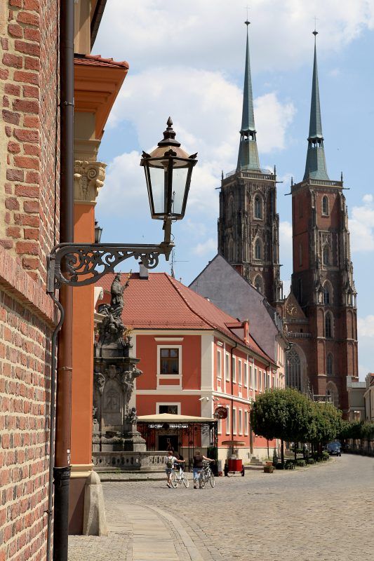 Latarnia gazowe na  zamontowana przy zabytkowej kamienicy, w tle widok na wysokie dwie wieże katedry