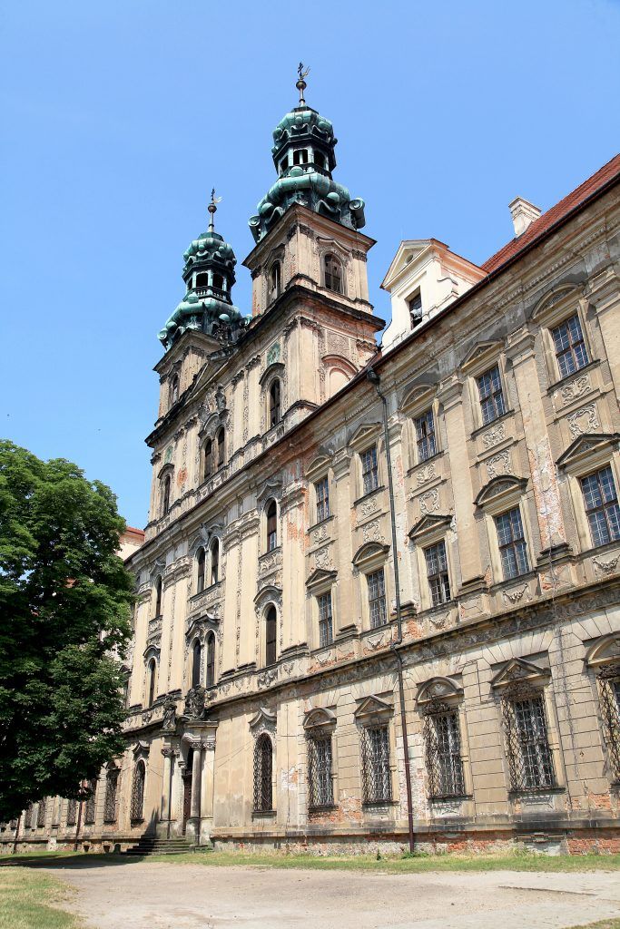 Barokowe mury opactwa zwieńczone dwiema wieżyczkami z dachem pokrytym seledynowym kolorem.