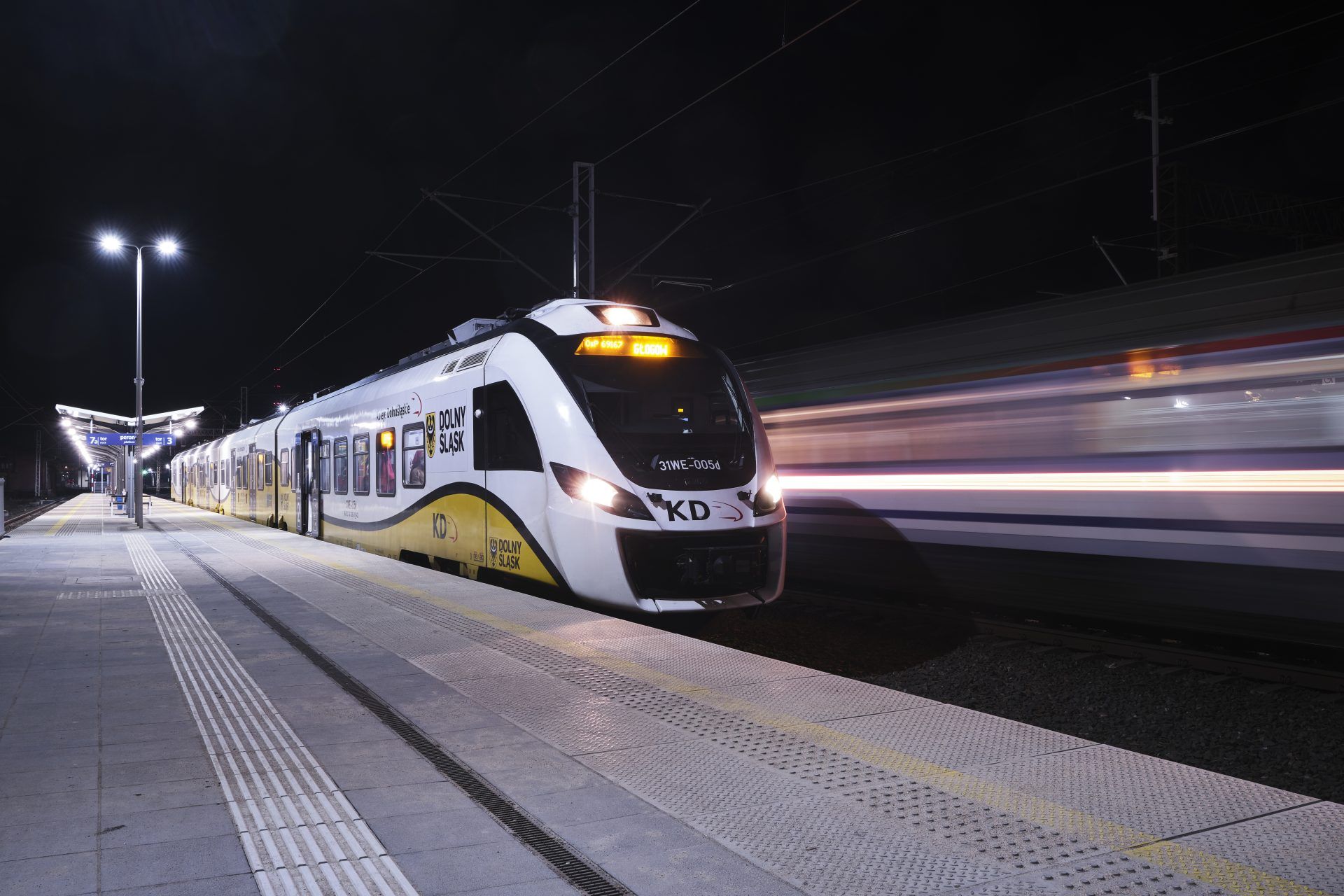 Pociąg kolej dolnośląskich mknący po torach przy peronie na tle nocnego nieba