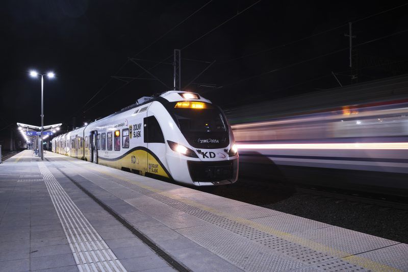 Pociąg kolej dolnośląskich mknący po torach przy peronie na tle nocnego nieba