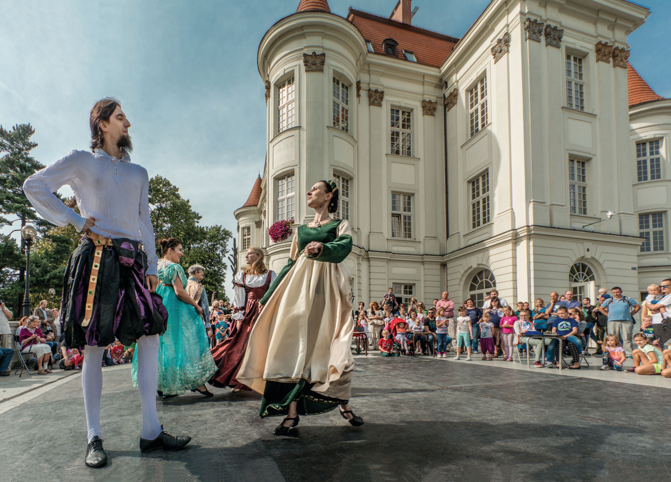 Tancerze na scenie w ludowych strojach na tle zamku i widzów