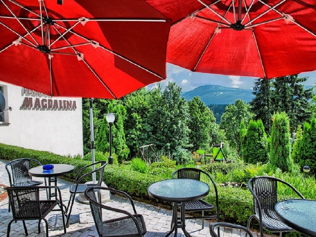Widok na taras wypoczynkowy ze stolikami i parasolami oraz górami w tle.