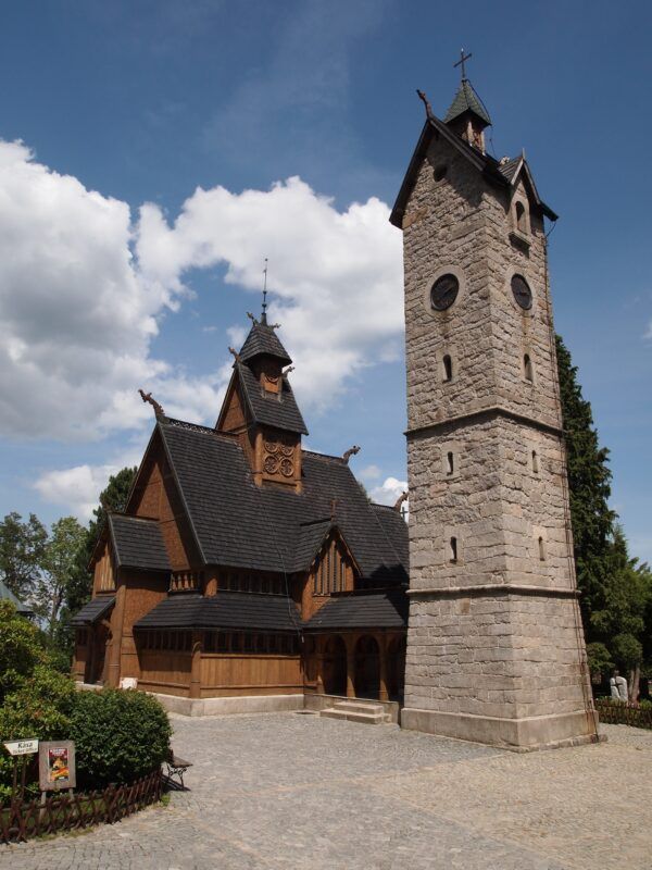 Widok na kościół na wzgórzu, wśród drzew. W tle błękitne niebo.