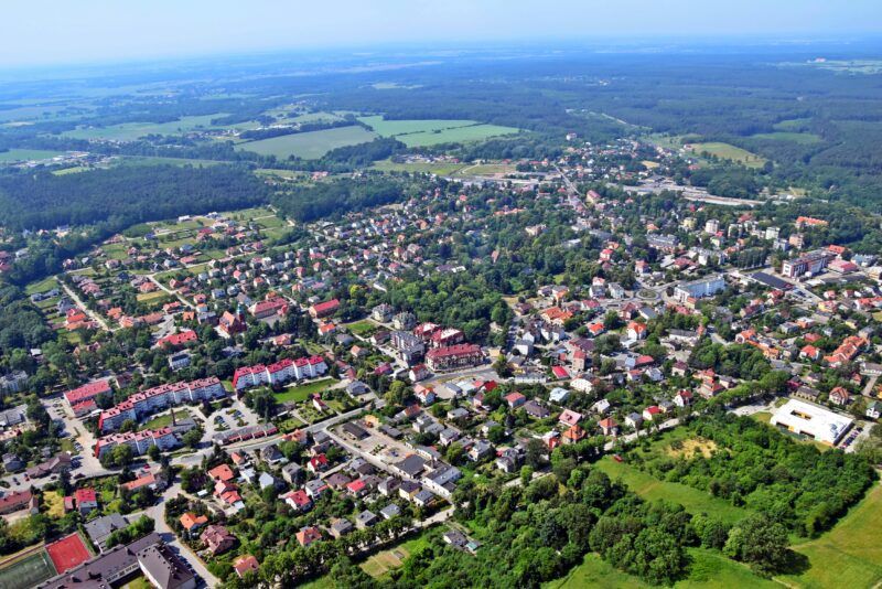 Panorama miasta z lotu ptaka na zdjęciu widoczne są infrastruktura miejska budowle itp. oraz otaczające miasto lasy
