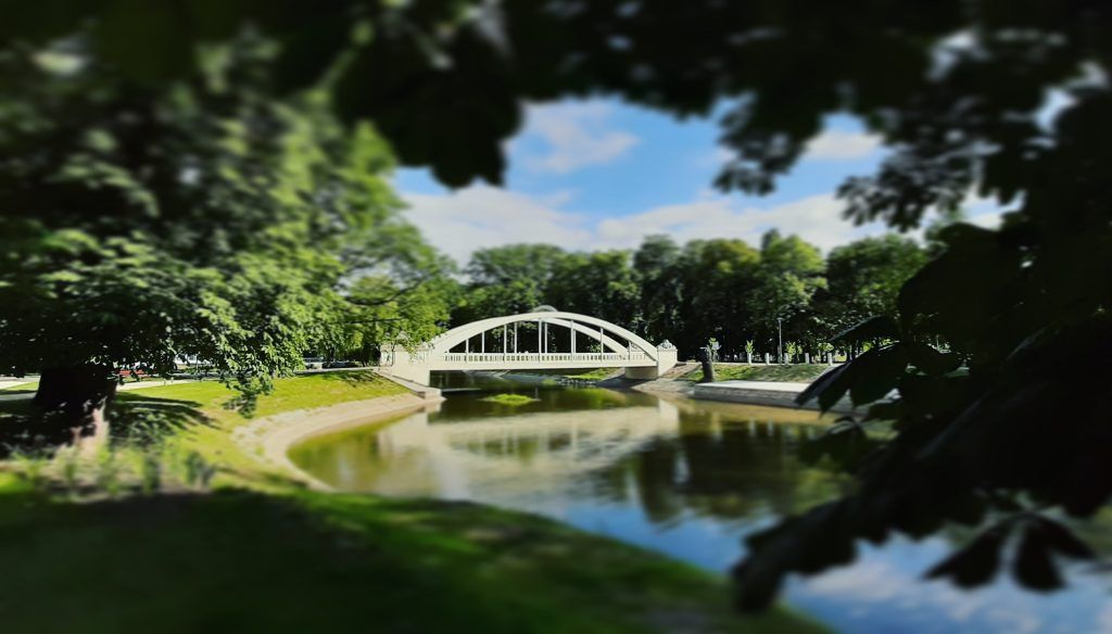 Most w jasnych barwach nad rzeką w otoczeniu zieleni