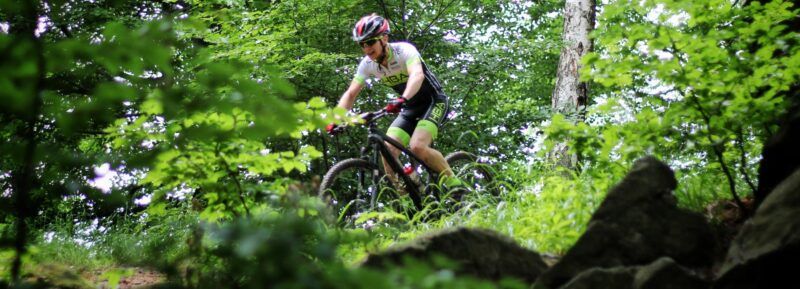 Rowerzysta w kasku na rowerze MTB jadący w nierównym terenie w lesie
