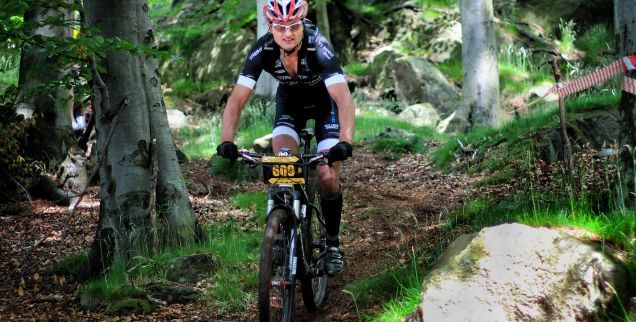 Rowerzysta w ubraniu sportowym i w kasku jadący na rowerze wyczynowym po leśnej ścieżce