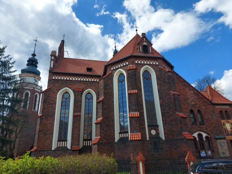 Kościół z wielkimi podłużnymi oknami z czerwonej cegły na tle jasnego nieba