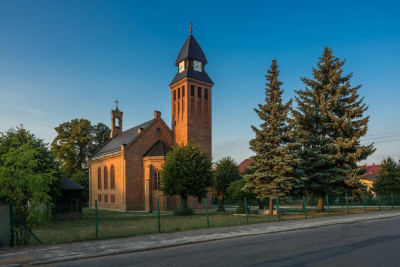 Kościół z cegły, otoczony drzewami, na tle błękitnego nieba.