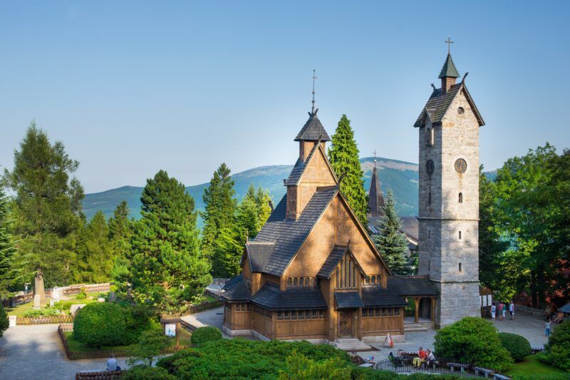 Widok na kościół na wzgórzu, wśród drzew. W tle góry oraz błękitne niebo.