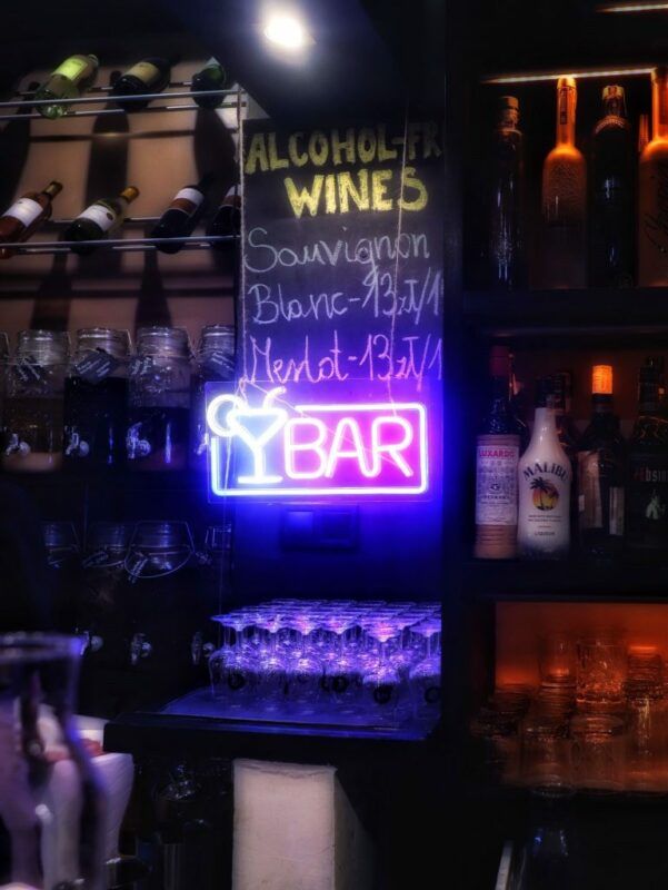 Bar w restauracji, butelki alkoholu na regałach oraz neon z napisem "BAR".