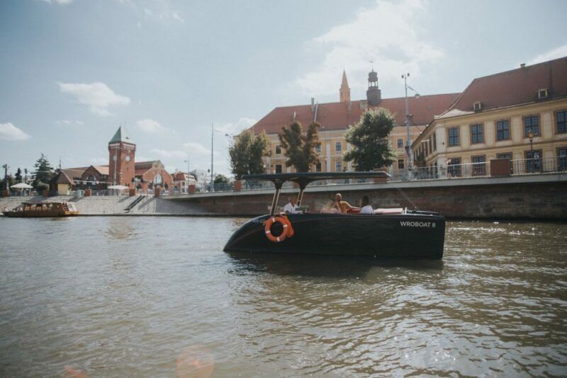Widok na rzekę Odrę i płynącą po niej łódź a w tle budynek Hali Targowej 