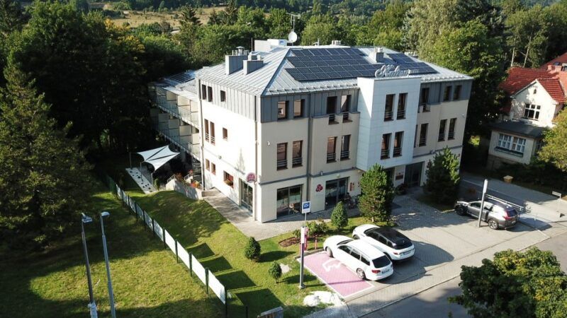 Duży nowoczesny budynek trójkondygnacyjny z przestronnym parkingiem przed wejściem.