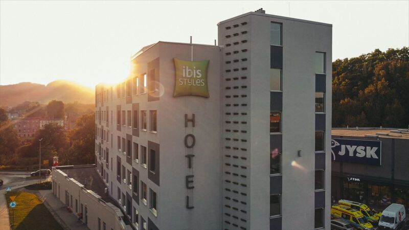 Wysoki, nowoczesny budynek hotelu z logiem na ścianie bocznej, na tle zachodzącego słońca. 
