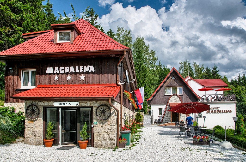 Widok na front budynku dwukondygnacyjnego, obitego drewnem, z kamienną podstawą. Nad wejściem napis Magdalena.