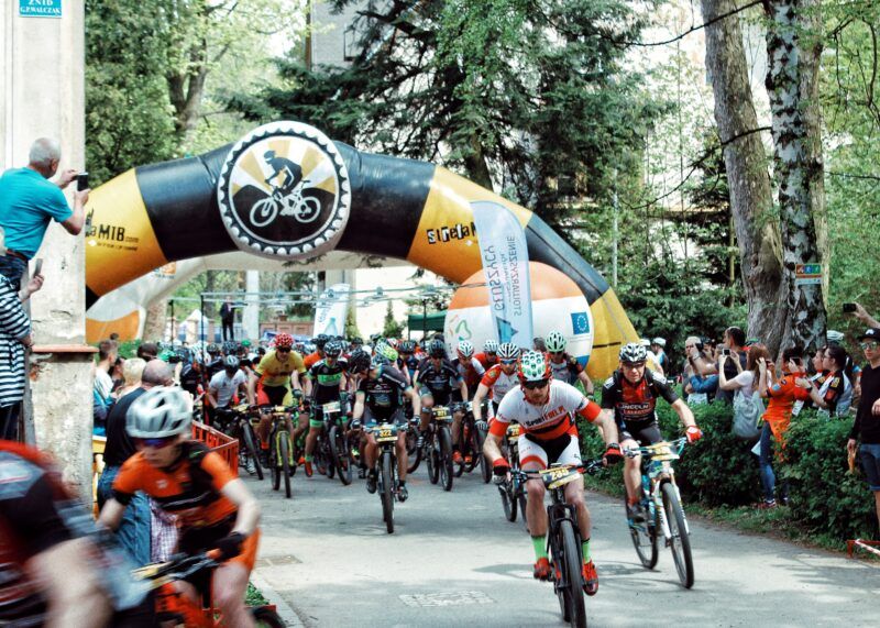 Rowerzyści biorący udział w wydarzeniu sportowym jadący na rowerach pośród kibicującej im publiczności