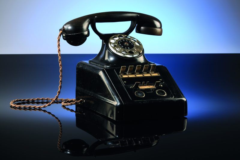 zdjęcie przedstawia czarny, stary telefon, stacjonarny na kabel, jest on oświetlany od tyłu niebieskim światłem