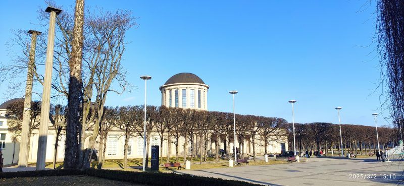 Modernistyczny budynek o prostych, geometrycznych kształtach, wyróżniający się czterema charakterystycznymi kopułami na dachu, otoczony przestronnym terenem.