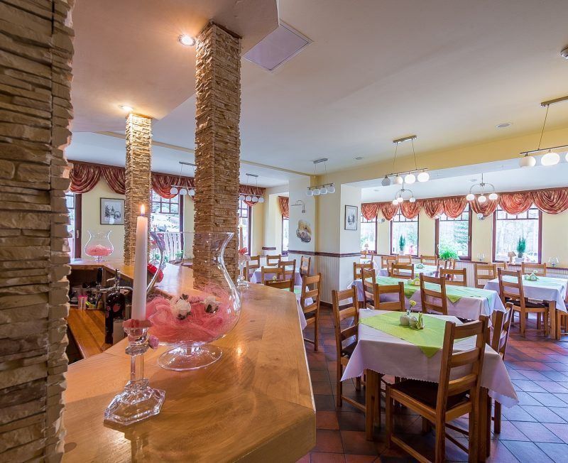 Restauracja hotelowa. Kwadratowe stoły nakryte białym obrusem, przy każdym po 4 drewniane krzesła.