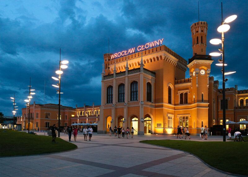 Budynek Dworca Głównego -  neogotycka konstrukcja z czerwonej cegły, charakteryzująca się wysoką wieżą zegarową, ozdobnymi detalami architektonicznymi oraz wieloma łukowymi oknami