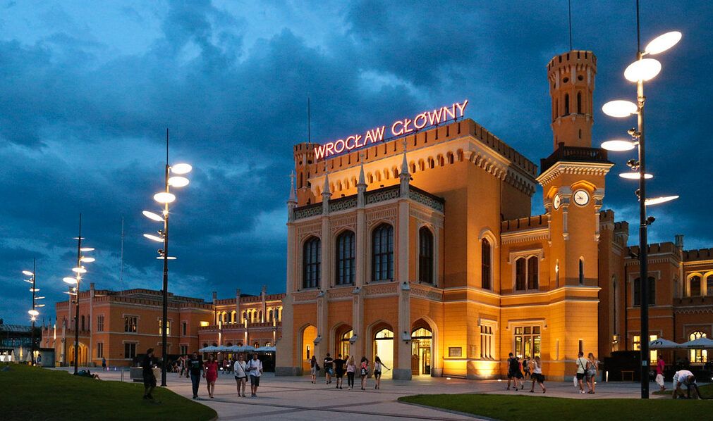 Budynek Dworca Głównego - neogotycka konstrukcja z czerwonej cegły, charakteryzująca się wysoką wieżą zegarową, ozdobnymi detalami architektonicznymi oraz wieloma łukowymi oknami