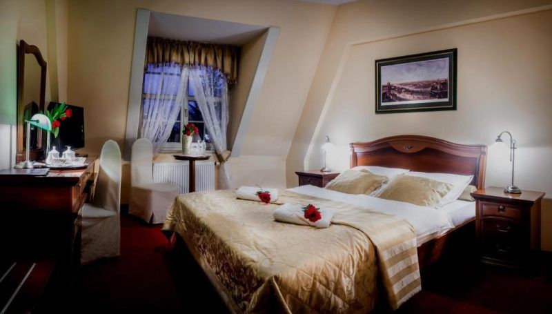 Elegancki, schludny pokój hotelowy z podwójnym łożem małżeńskim, komodą oraz krzesłem, dwoma szafkami nocnymi z lampkami i 