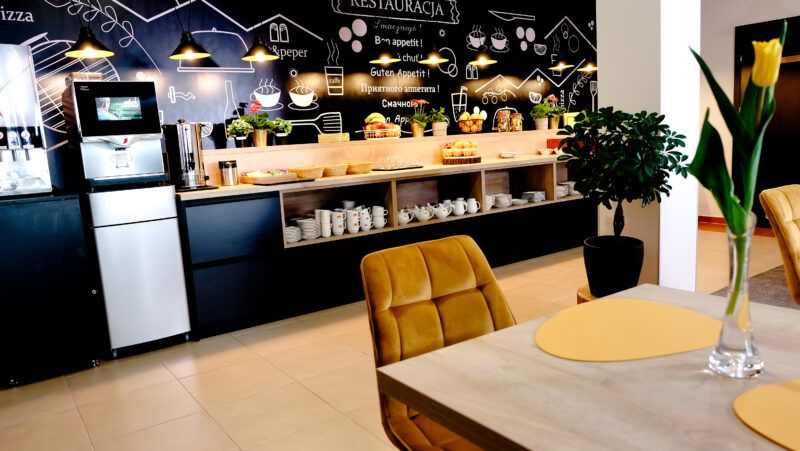Restauracja hotelowa w stylu nowoczesnym z dominantą czerni. Na ścianie nad samoobsługowym bufetem tablica z napisami z kredy z dostępnym menu.
