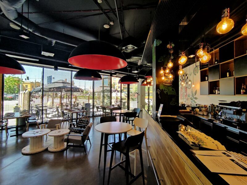 Nowoczesne, designerskie wnętrze sali restauracyjnej. Dekorację stanowią elementy industrialne (widoczne rury wentylacyjne na suficie oraz duże szpule na druty zamiast stolików).