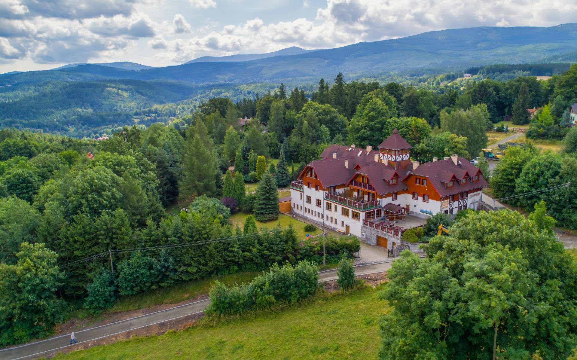 Duży budynek hotelowy w pięknym otoczeniu letniego krajobrazu i zieleni w pełnym rozkwicie, na tle gór. 