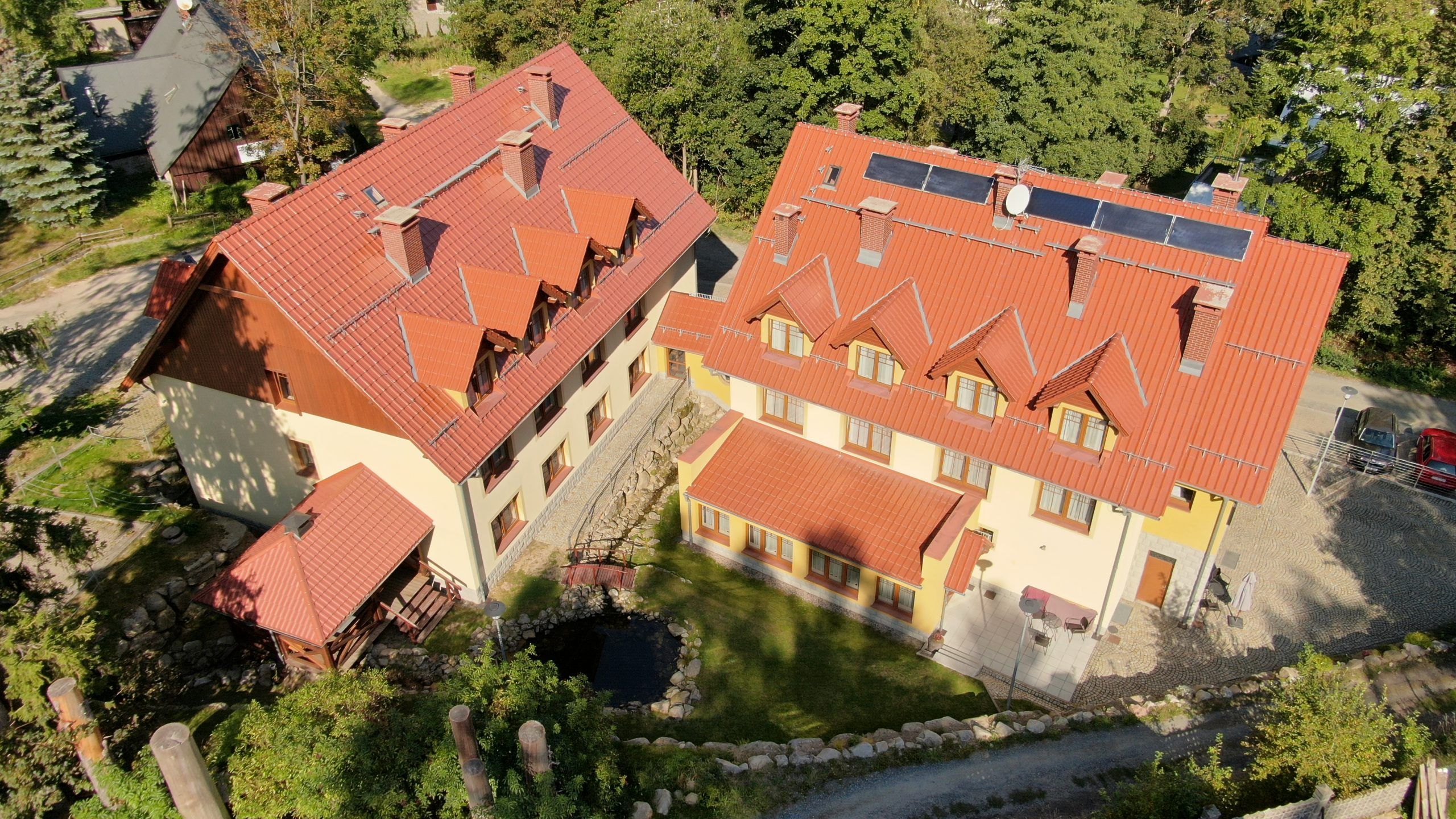 Zdjęcie z drona przedstawiające szczyty dwóch przylegających do siebie budynków hotelowych, ulokowanych w zielonej okolicy