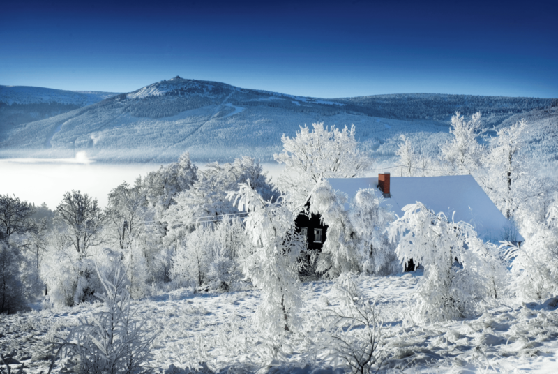 Zdjęcie domu z dwuspadowym dachem z widoczną górą Szrenicą w tle na tle bechmurnego nieba