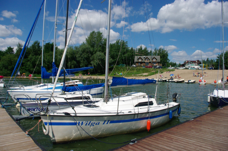 Widok na łódki przy pomoście, w tle plaża i drzewa.