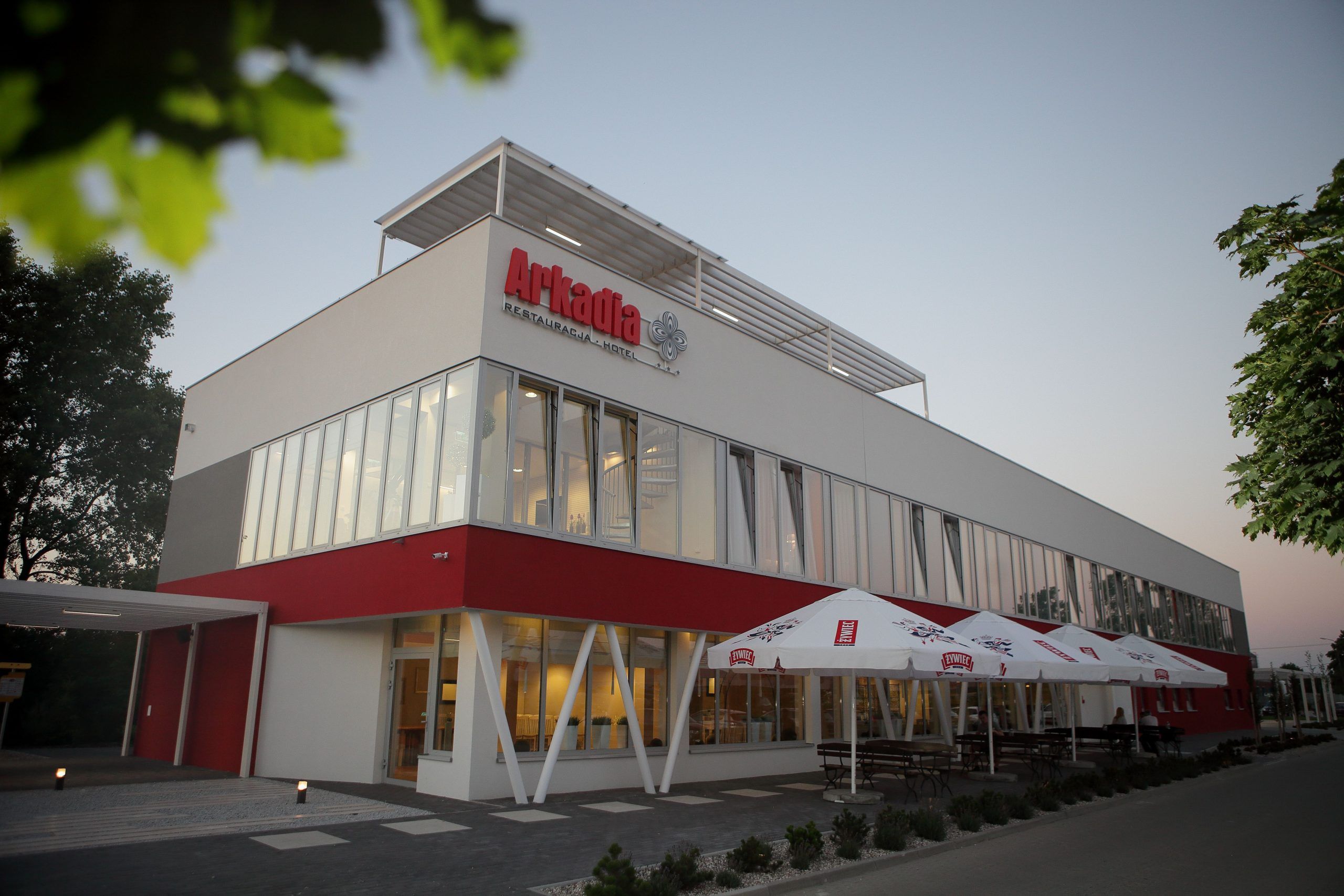 Nowoczesny budynek hotelu, przed którym stoi rząd dużych parasoli ogrodowych. 