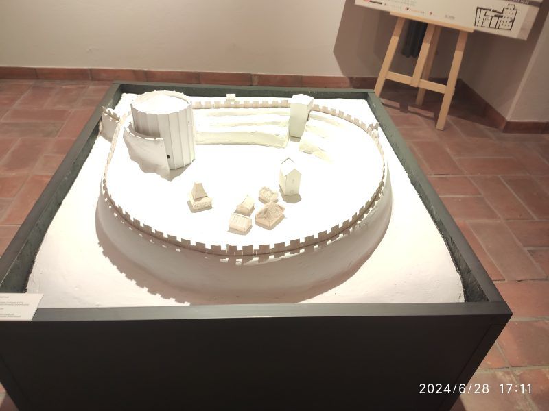 Pierwsze zdjęcie przedstawia makietę dawnej budowli obronnej z murami i wieżą. Model pokazuje układ fortyfikacji i zabudowań wewnątrz.
