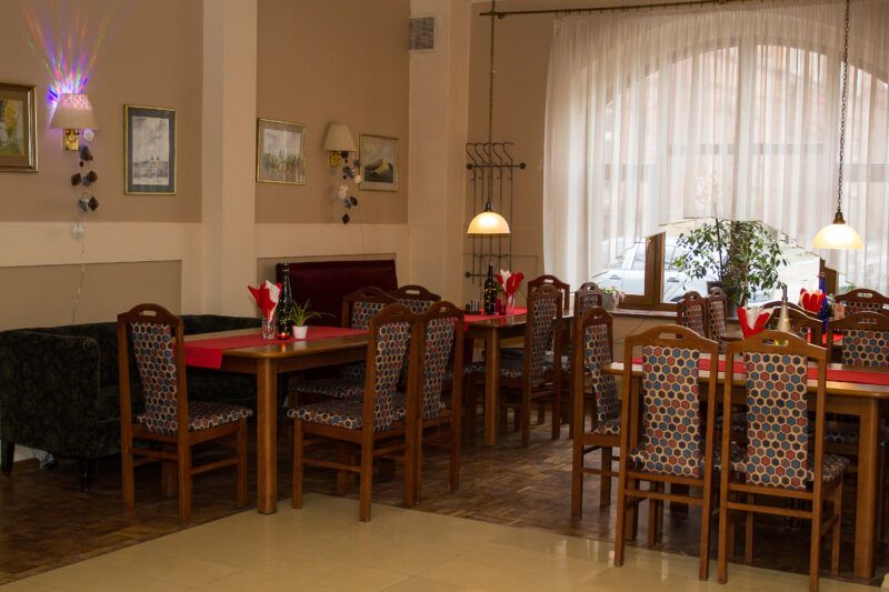 Sala jadalna z kilkoma stołami, przy których, przy każdym stoi od 4 do 6 krzeseł