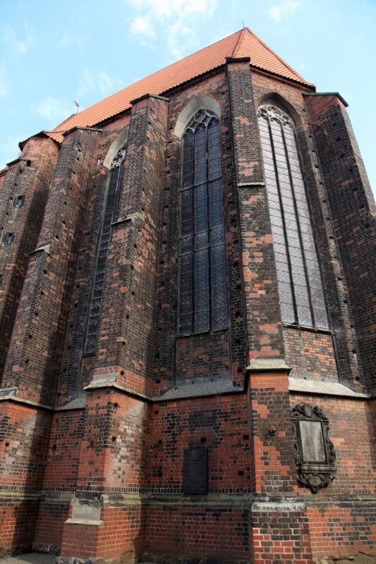 Gotycka budowla z cegły, z charakterystyczną smukłą wieżą, ostrołukowymi oknami oraz prostą, ale elegancką bryłą, udekorowaną detalami architektonicznymi