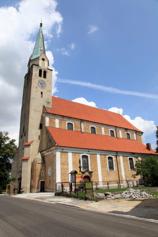 Budowla z kamienia, charakteryzująca się wysoką, smukłą wieżą, ostrołukowymi oknami oraz prostą, ale elegancką bryłą, otoczoną ceglanym murem.
