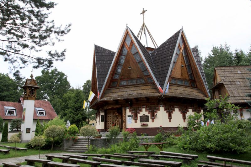 Niewielka, neogotycka budowla z cegły, z charakterystycznym, ostrym dachem i detalami architektonicznymi, otoczona zielenią